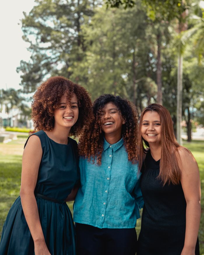 Three cheerful women of diverse backgrounds smiling together in a Brazilian park.